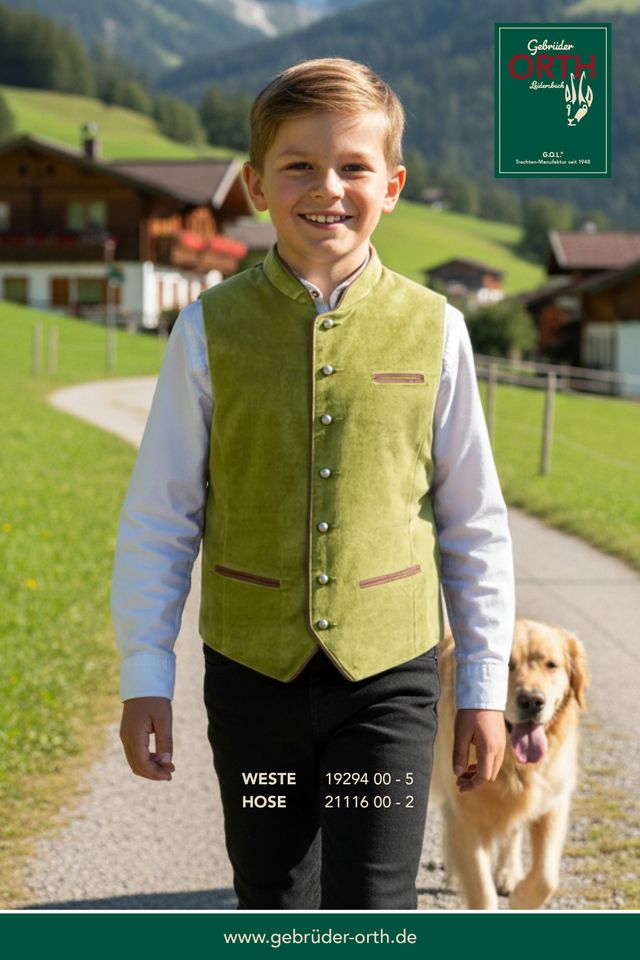 Junge in grüner Weste mit Hund vor alpiner Landschaft, lächelnd.