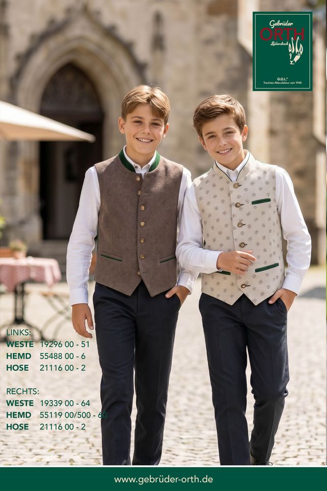 Zwei Jungen in traditioneller Tracht mit Weste und Hemd vor historischer Architektur.