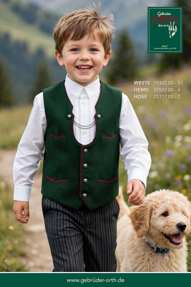 Junge mit Hund in traditioneller Tracht, lächelnd in blühender Landschaft.