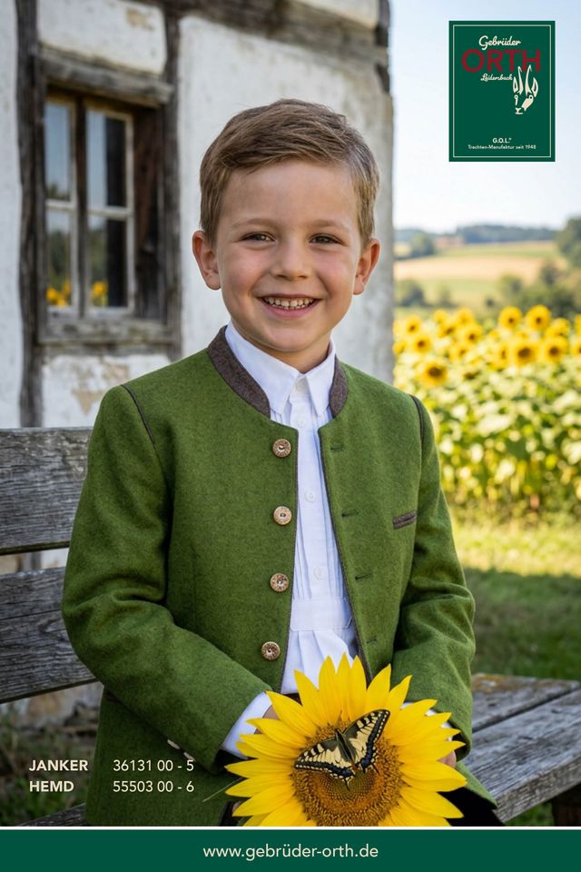 Glücklicher Junge in Trachtjacke hält Sonnenblume, lächelt vor ländlicher Kulisse.