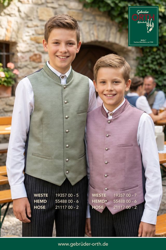 Zwei Jungen in traditionellen Hemdenwesten, lächeln vor rustikalem Hintergrund.