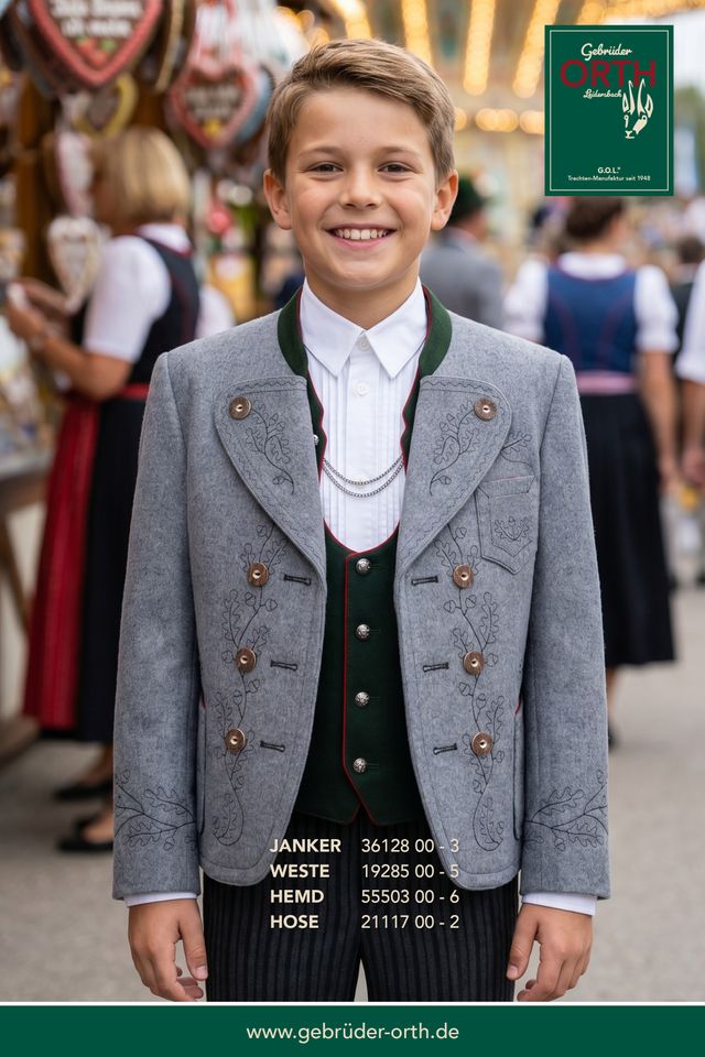 Junge in traditioneller Tracht mit grauer Jacke, weißem Hemd und Weste, lächelnd auf Volksfest.