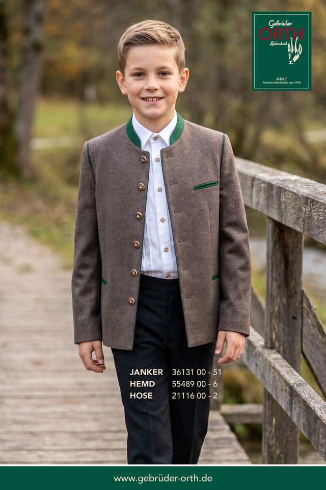 Junge trägt traditionelle Lederhose mit Weste, Hemd und Jacke auf Holzbrücke.