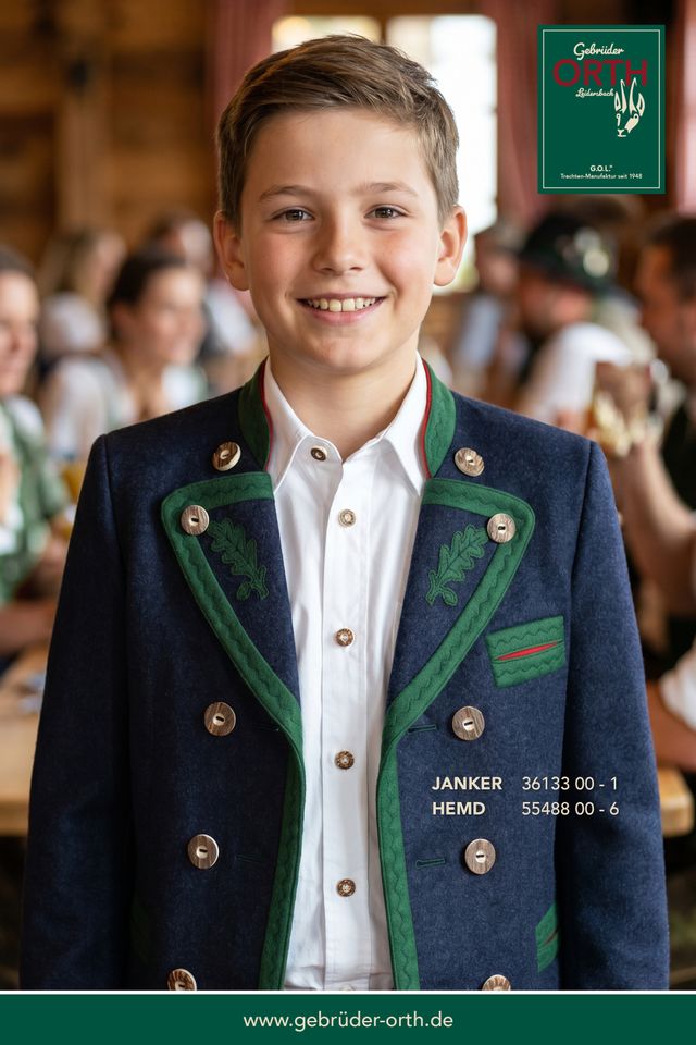 Junge in traditioneller Trachtjacke mit glücklichem Lächeln bei einer Veranstaltung.