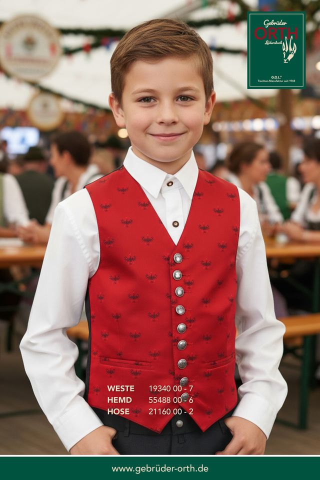 Junge in traditioneller Tracht mit roter Weste und weißem Hemd, lächelnd im Festzelt.