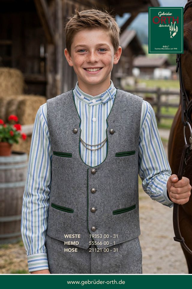 Junge in traditioneller Tracht mit Weste, Hemd und Hose, lächelnd vor Pferden.